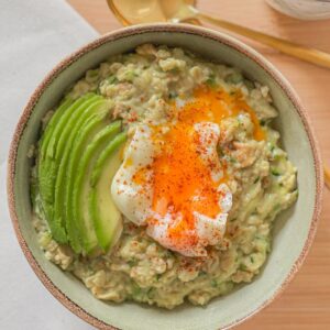 A comforting bowl of savory oatmeal topped with poached egg, sliced avocado, and chili flakes for extra flavor