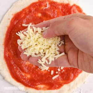 Sprinkling low fat shredded cheese (mozzarella) on top of a low calorie pizza crust spread with tomato sauce