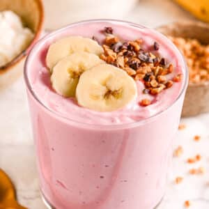A creamy strawberry cottage cheese smoothie in a glass, topped with banana slices and crunchy cacao nibs.