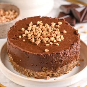 Chocolate healthy cheesecake topped with chopped nuts on a white plate, featuring a no-bake oat crust and creamy Greek yogurt filling.