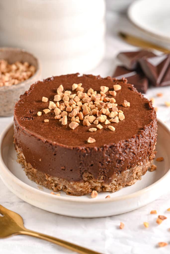 Chocolate healthy cheesecake topped with chopped nuts on a white plate, featuring a no-bake oat crust and creamy Greek yogurt filling.