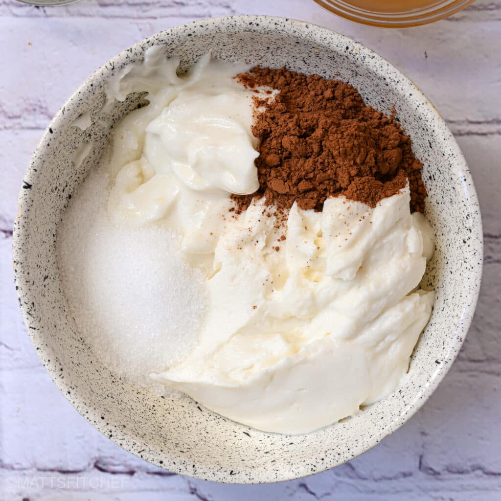 Mixing Greek yogurt cheesecake filling with cocoa powder and sweetener in a bowl.