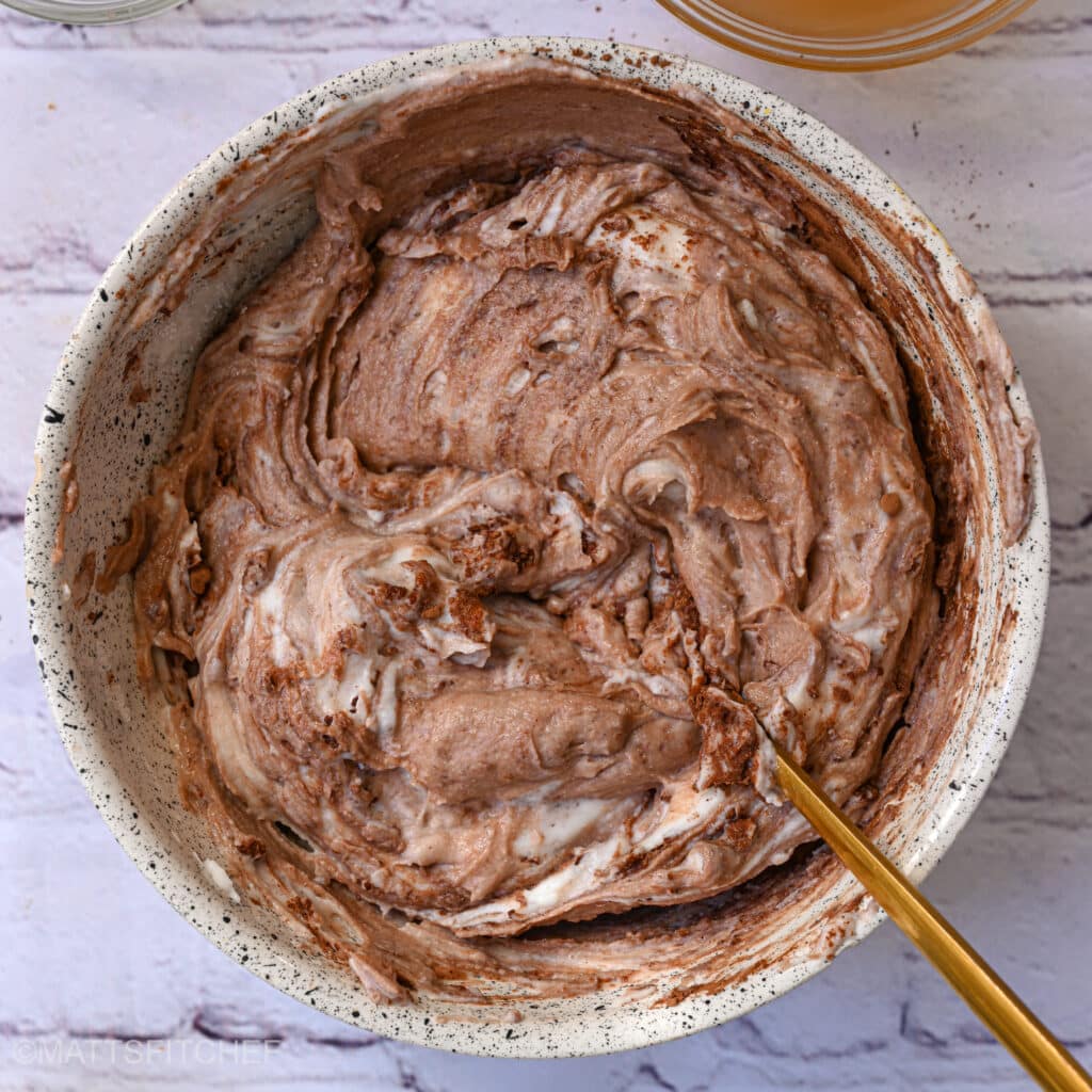 Swirled chocolate cheesecake batter in a mixing bowl, made with Greek yogurt and cream cheese.