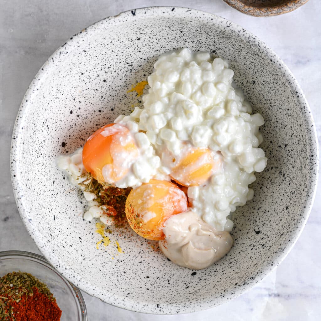 Egg yolks mixed with cottage cheese, Dijon mustard, and seasonings in a bowl.