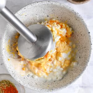 A hand blender mashing cottage cheese and yolks for a protein deviled egg filling.