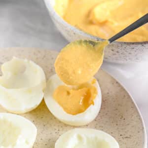 A spoon scooping the yolk mixture into egg whites for deviled eggs.