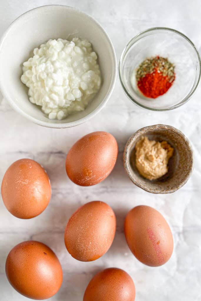 Ingredients for healthy deviled eggs – Brown eggs, cottage cheese, Dijon mustard, and seasonings arranged on a marble surface.