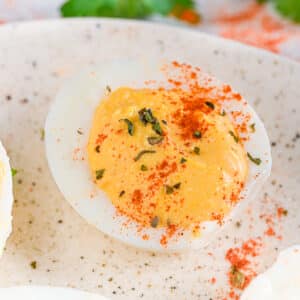 Cottage cheese deviled egg on a plate - A healthy deviled egg sprinkled with smoked paprika and dried herbs on a ceramic plate.