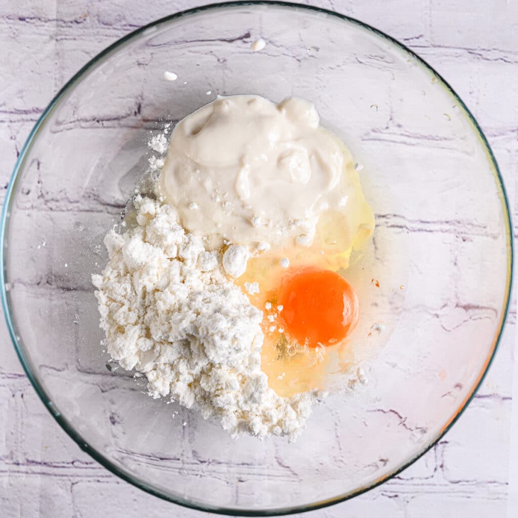 A glass bowl with protein powder, Greek yogurt, and an egg, ready to make high-protein pancakes.