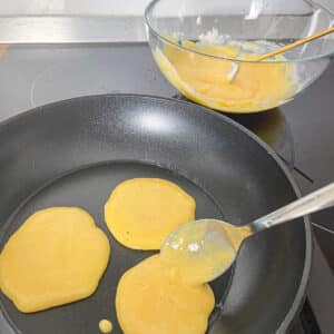 Pouring Pancake Batter into a Pan – A spoon spreading protein pancake batter onto a non-stick skillet.