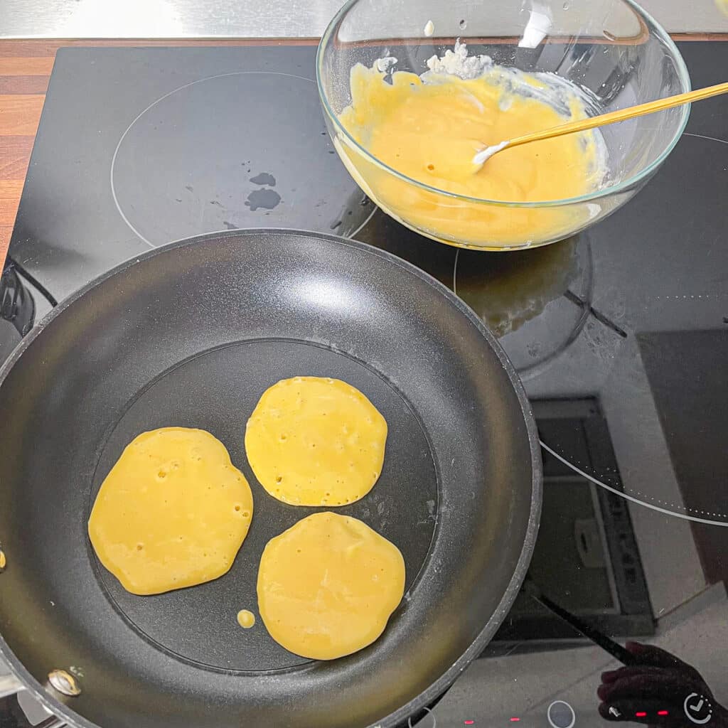 Cooking Protein Pancakes on a Skillet – Three protein pancakes cooking on a stovetop over medium heat.