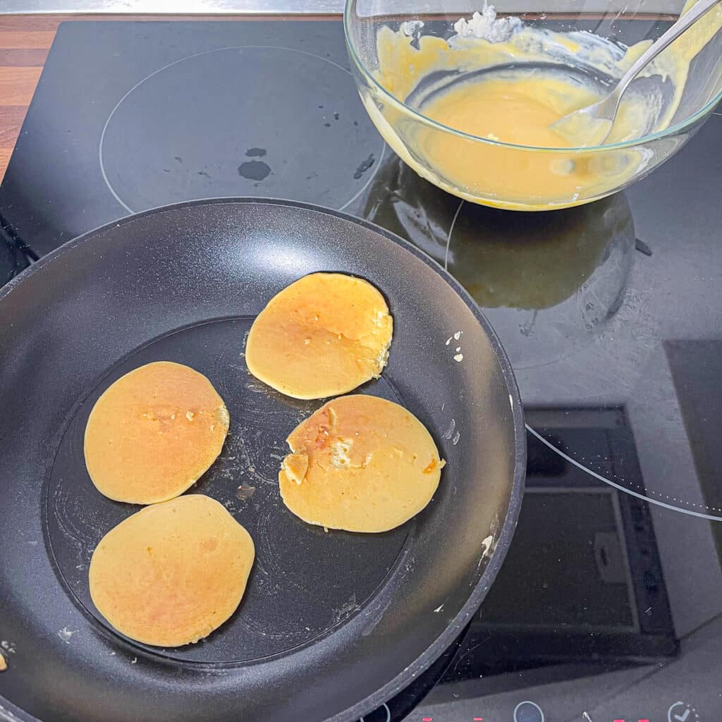 Flipping Protein Pancakes – Golden-brown protein pancakes being flipped in a non-stick frying pan.