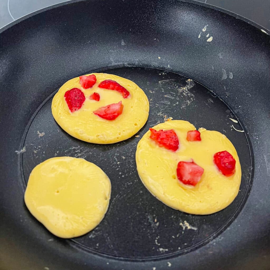 Protein pancakes with strawberries - Adding strawberries to pancakes while cooking.