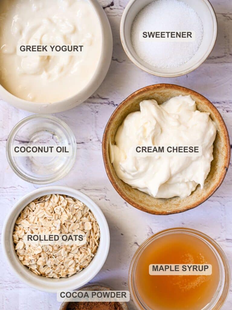 Healthy cheesecake ingredients laid out, including Greek yogurt, cream cheese, oats, cocoa powder, and natural sweeteners.