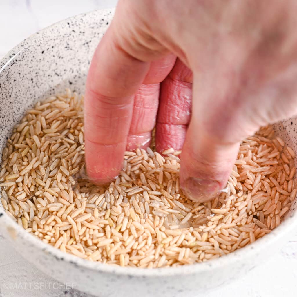 Hand rinsing uncooked brown rice in a ceramic bowl for better texture.