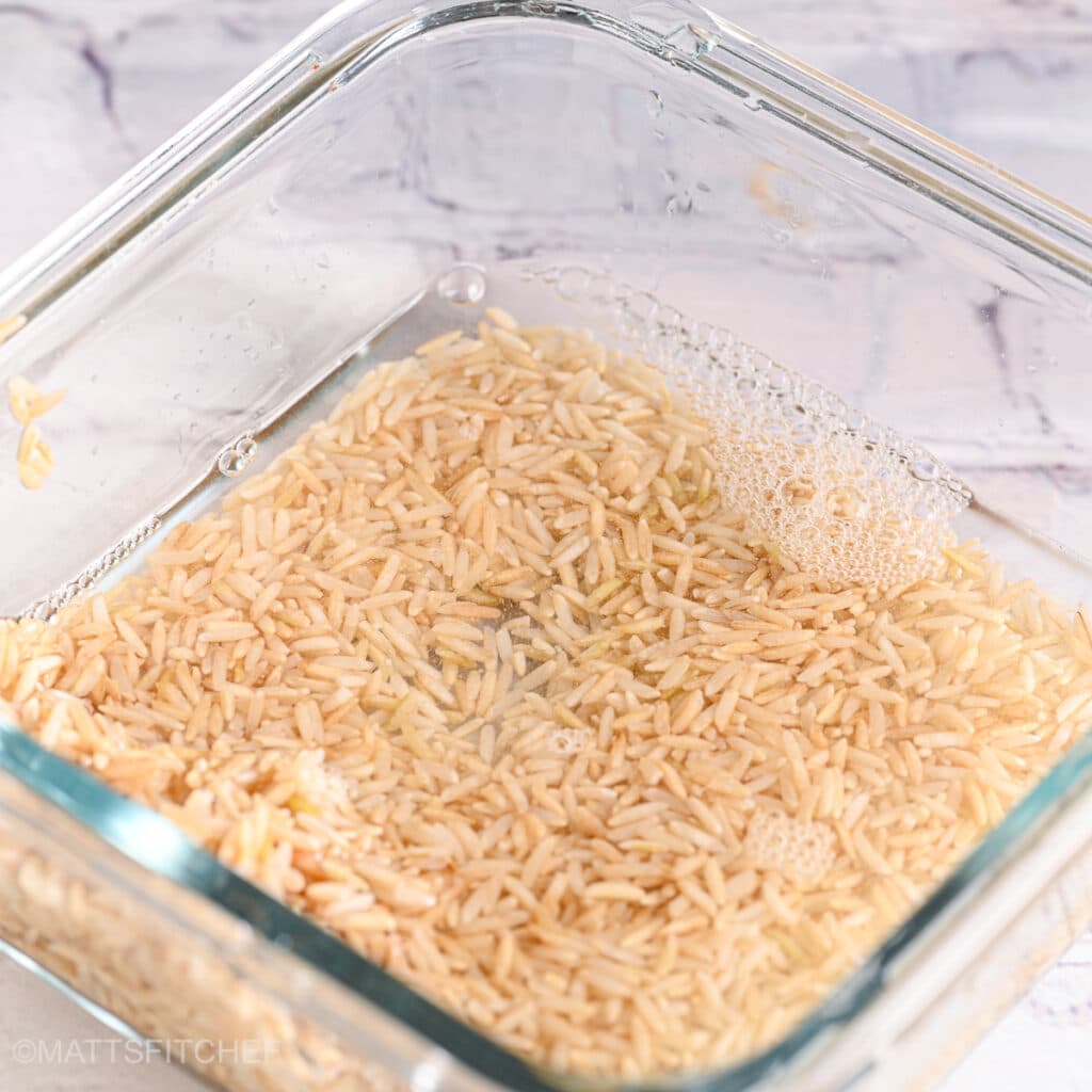 Rice covered in water in a glass bowl for cooking.