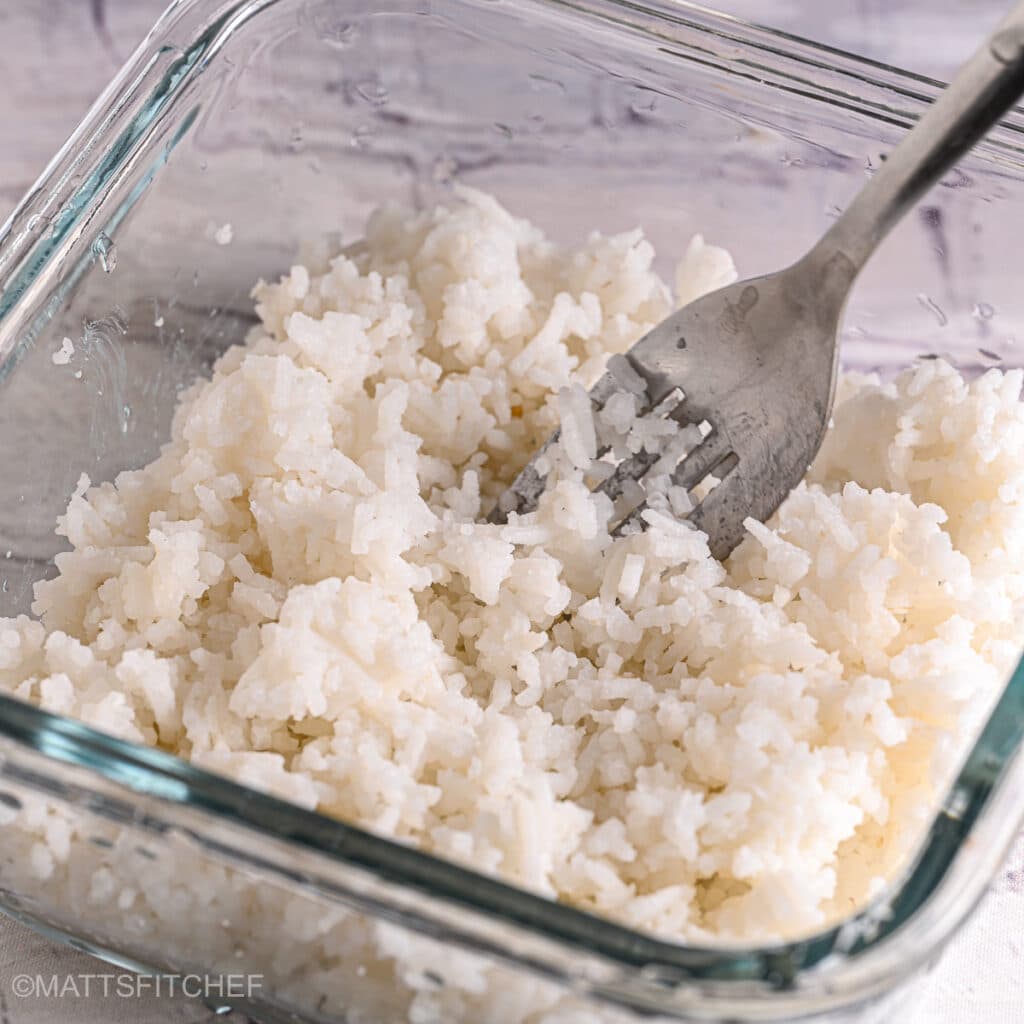 Fluffing freshly microwaved white rice with a fork in a glass container.