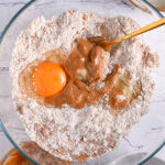 A mixture of almond flour, protein powder, peanut butter, eggs, and sweetener ready to be combined for the perfect protein cookie dough.