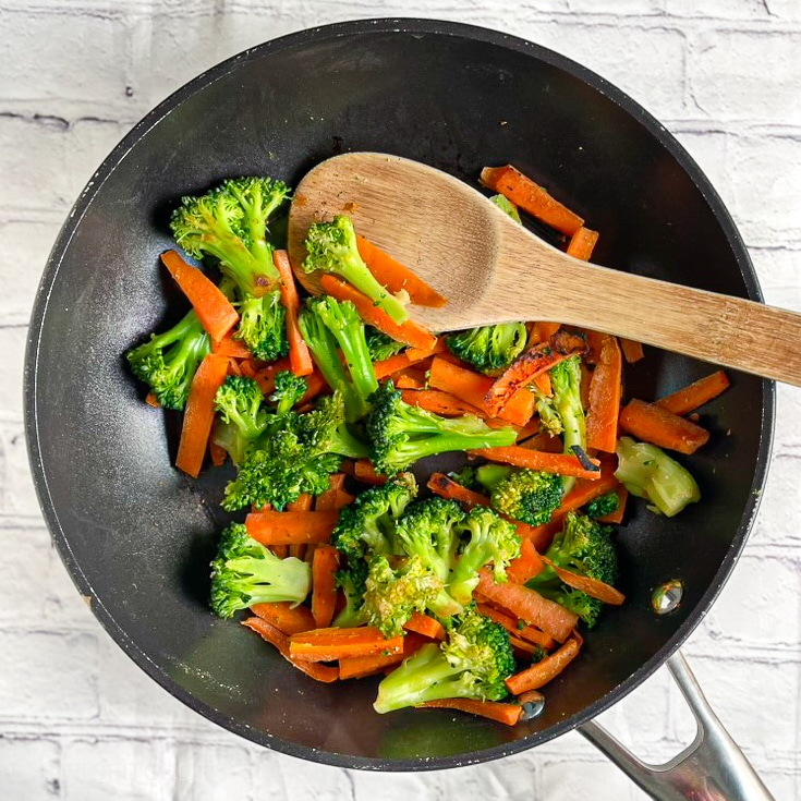 Freshly sautéed broccoli and carrots in a black wok, ready for tofu stir fry.