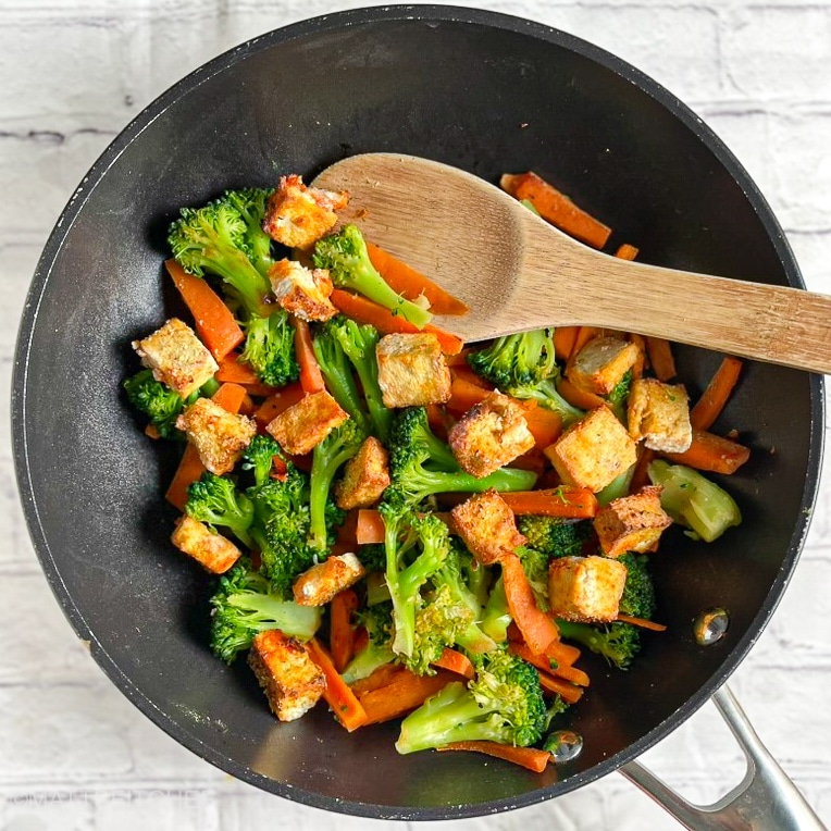 Golden-brown crispy tofu tossed with stir-fried broccoli and carrots in a wok.