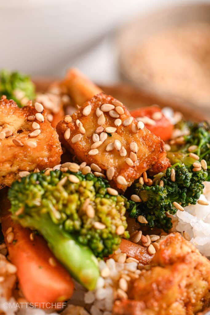 Closeup of a crispy stir fried tofu cube topped with sesame seeds over a bowl of basmati rice.