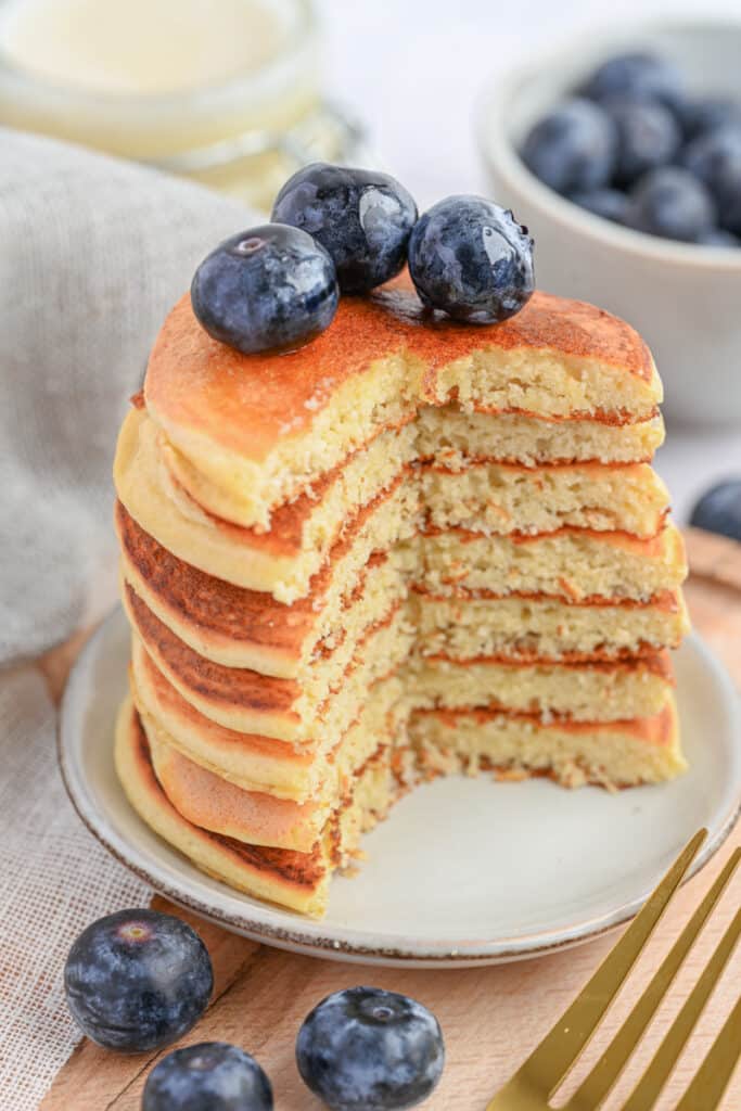 A tall stack of golden, fluffy protein pancakes with protein powder topped with fresh blueberries.