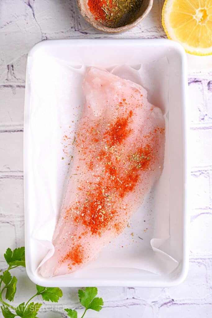 Seasoned cod fillet before baking – Cod fillet sprinkled with smoked paprika and herbs in a baking dish, prepped for the oven.