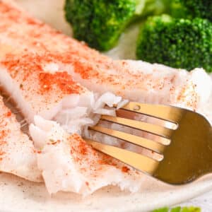 Fork flaking baked cod fillet – A fork breaking apart a flaky, moist cod fillet, showing its delicate texture.