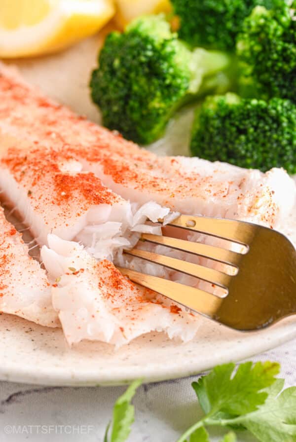 Fork flaking baked cod fillet – A fork breaking apart a flaky, moist cod fillet, showing its delicate texture.