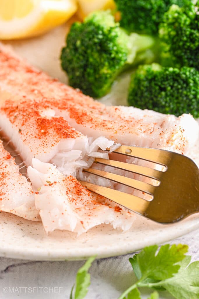 Fork flaking baked cod fillet – A fork breaking apart a flaky, moist cod fillet, showing its delicate texture.