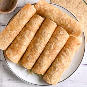 A full plate of rolled, uncooked chicken taquitos made with whole wheat tortillas, ready to cook.