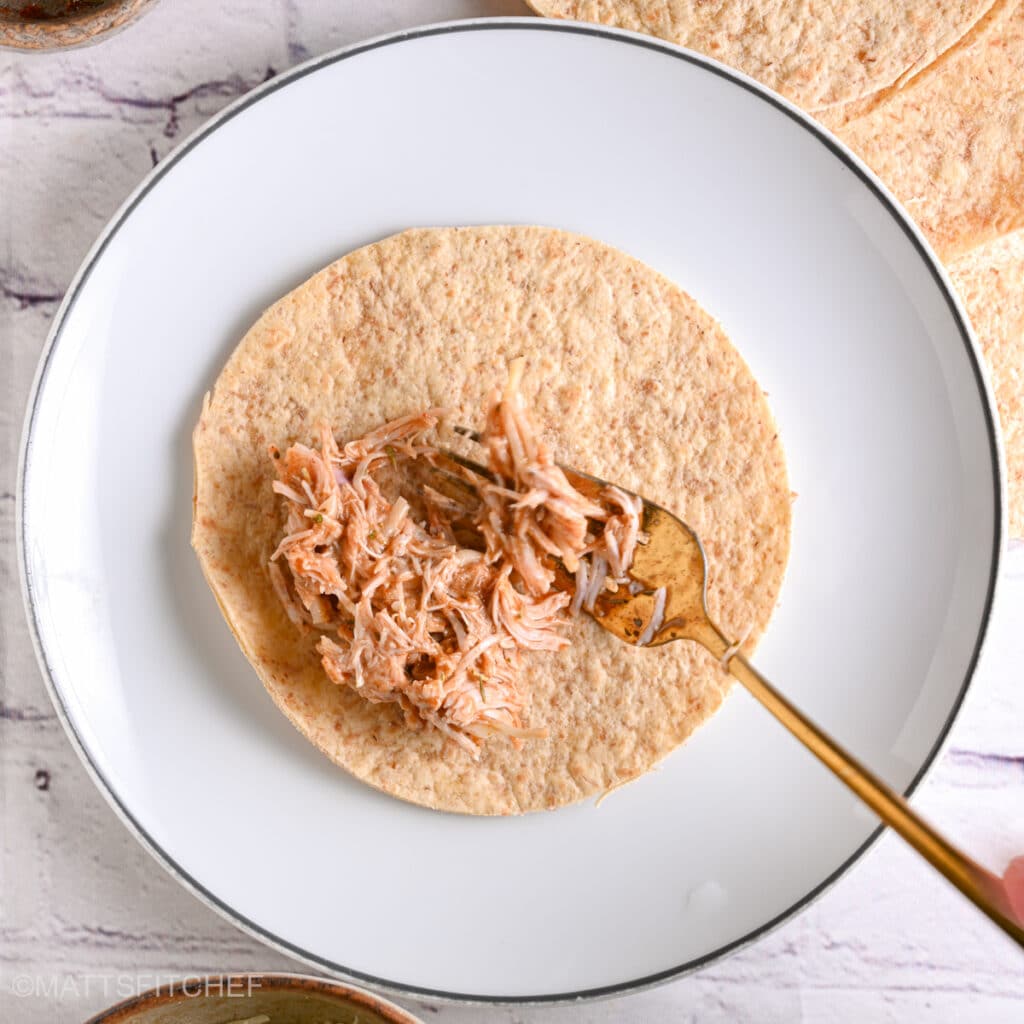 Spooning shredded chicken filling onto a tortilla to roll homemade chicken taquitos.