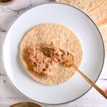 Spooning shredded chicken filling onto a tortilla to roll homemade chicken taquitos.
