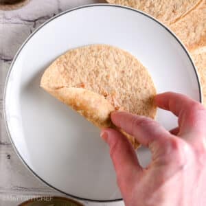 Folding the tortilla over the chicken mixture to start rolling a taquito tightly.
