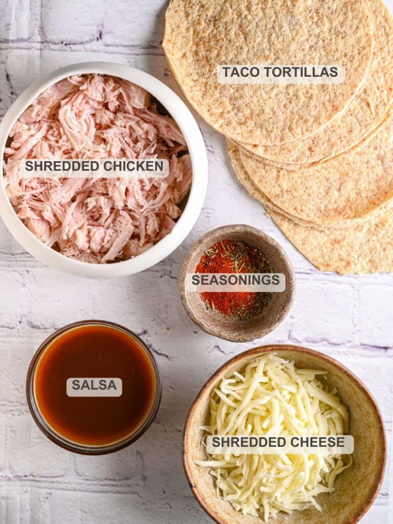 Overhead photo of chicken taquito ingredients: shredded chicken, tortillas, salsa, shredded cheese, and seasoning