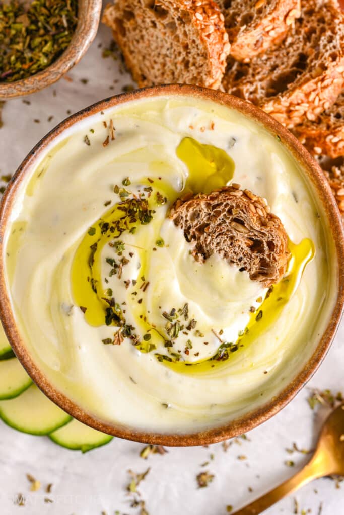 Thick and smooth whipped cottage cheese dip with golden olive oil, paired with crunchy seeded bread and fresh vegetables.