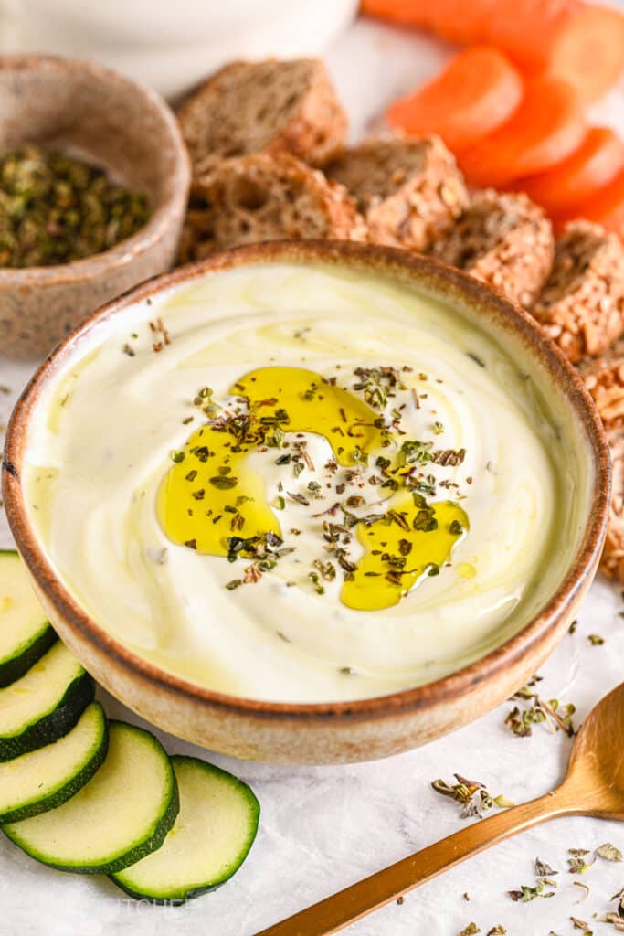 High-protein cottage cheese dip garnished with herbs and olive oil, perfect for dipping with bread, carrots, and zucchini.