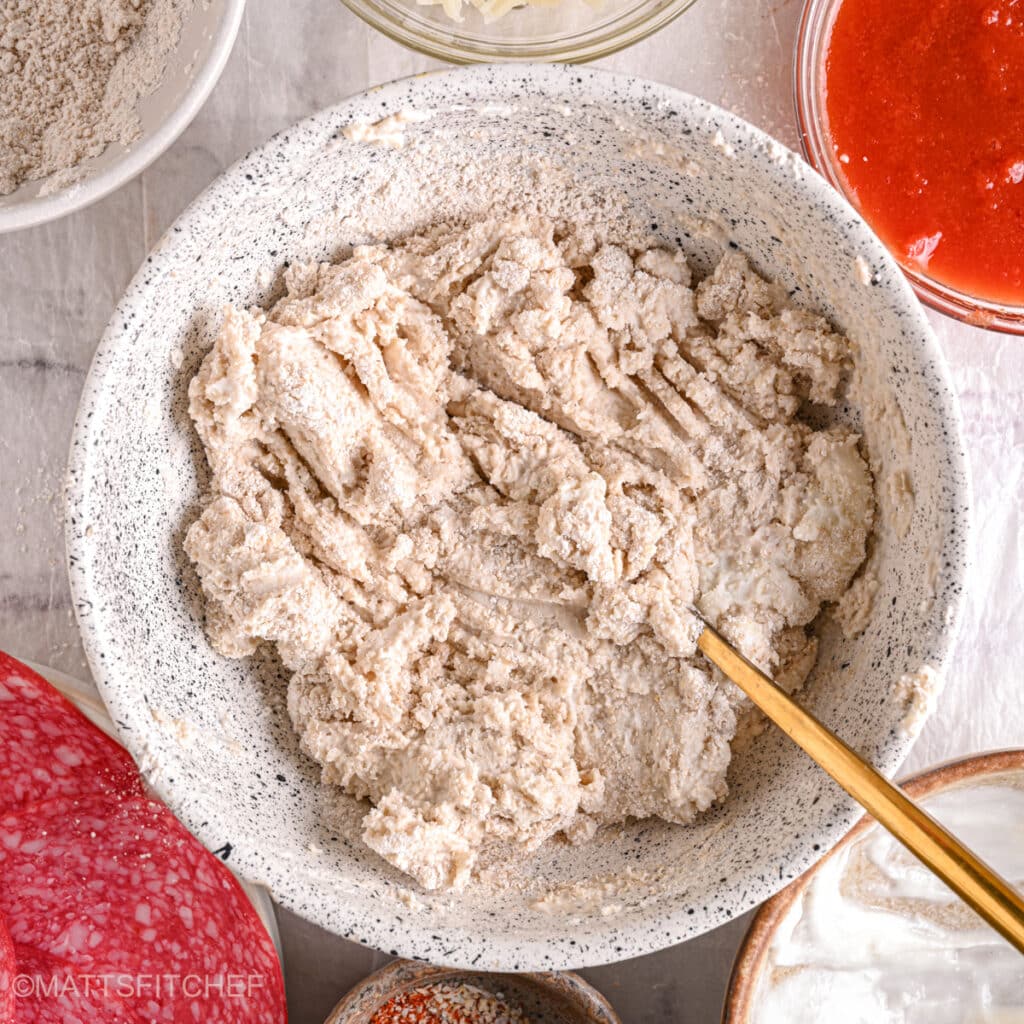 Thick pizza dough mixture – A soft, sticky dough forming as cottage cheese, whole wheat flour, and baking powder combine.