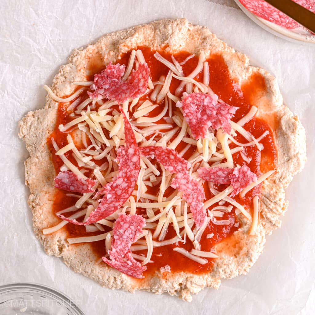 Topping pizza with turkey salami – Lean turkey salami slices added to a protein-rich, low-carb pizza crust before baking.