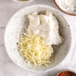 Shredded cheese added to cottage cheese – A bowl with shredded cheese on top of blended cottage cheese, ready to be mixed.