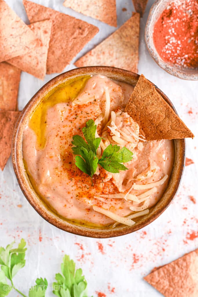 Dipping a chip into cottage cheese queso &ndash; A crispy pita chip scooping up creamy, high-protein queso.