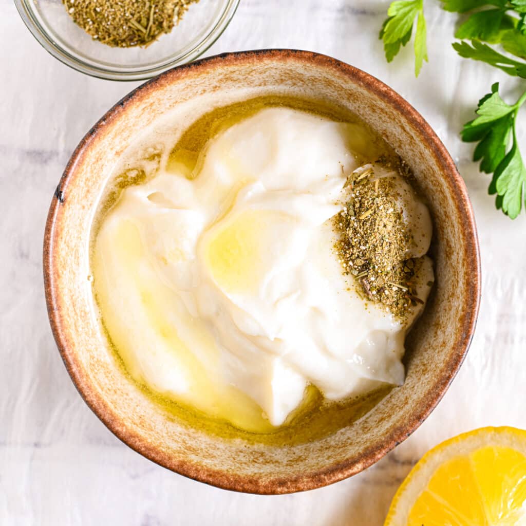 A bowl of Greek yogurt with olive oil and dried herbs, the key ingredients for homemade ranch dressing.