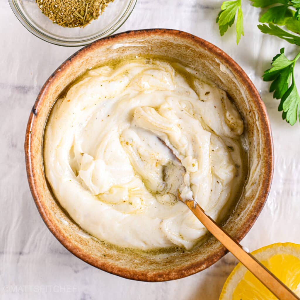 Mixing Greek yogurt ranch dressing with a spoon, blending olive oil and seasonings for a smooth texture.