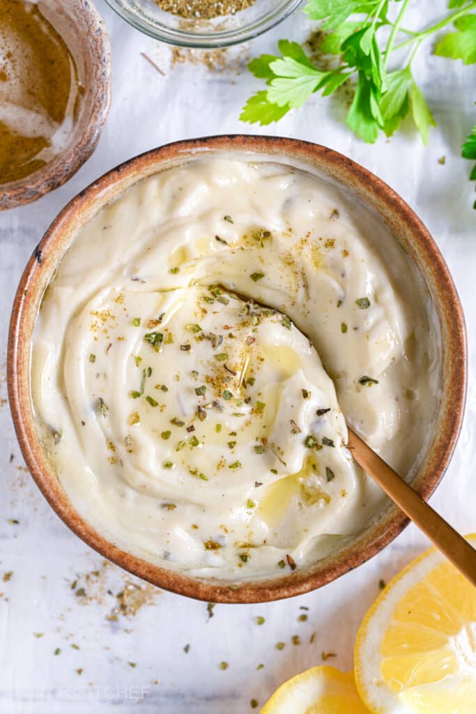 Finished Greek yogurt ranch dressing with olive oil drizzle and herbs, served in a bowl with fresh parsley and lemon slices.