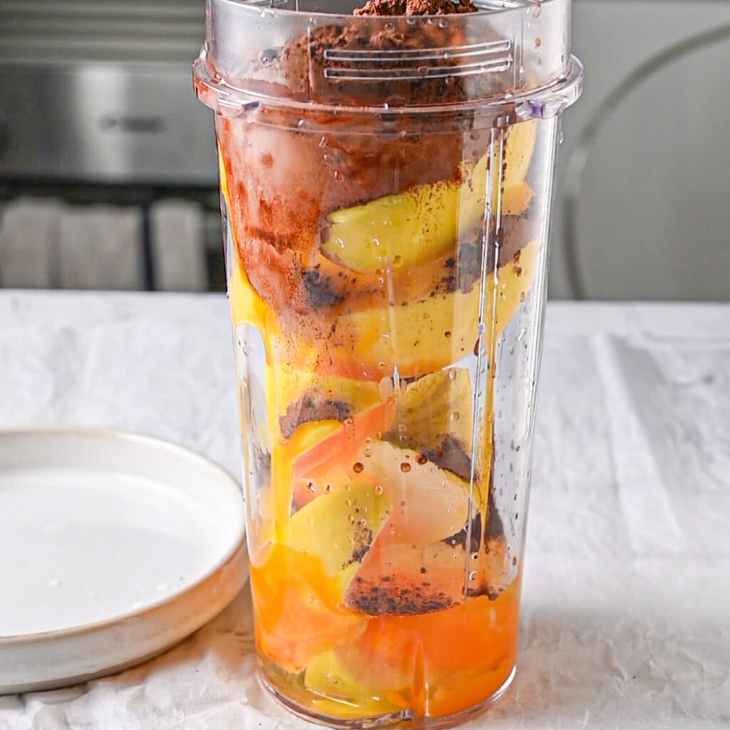 Blender filled with apples, egg, and cocoa powder for a healthy low calorie mug cake.