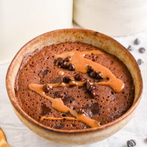 Healthy chocolate mug cake topped with melted peanut butter and chocolate chips.