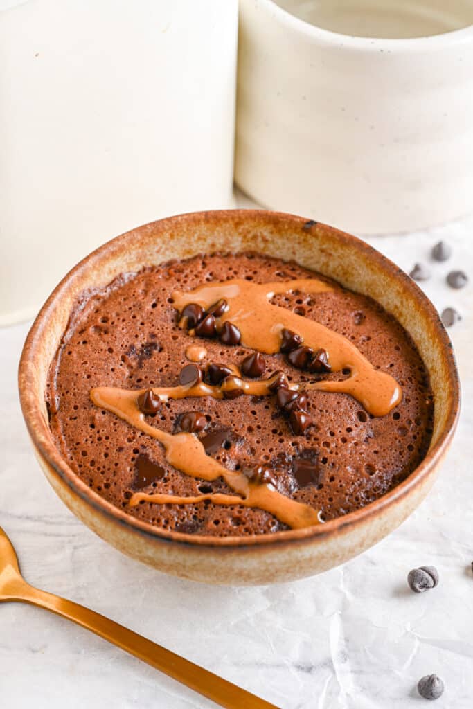 Healthy chocolate mug cake topped with melted peanut butter and chocolate chips.