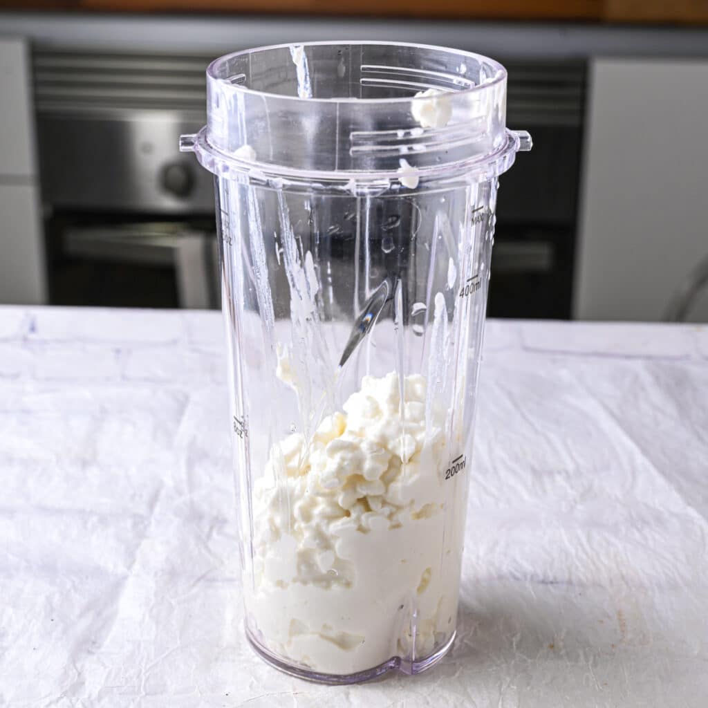 Blender cup filled with plain cottage cheese, the base ingredient for making homemade protein ice cream.
