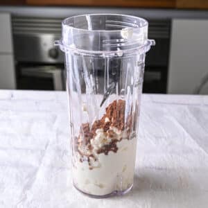 Blender cup filled with cottage cheese and cocoa powder, ready to be blended for homemade high-protein chocolate dessert.