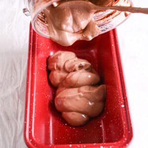 Thick and creamy chocolate cottage cheese ice cream being poured from a blender into a red loaf pan.